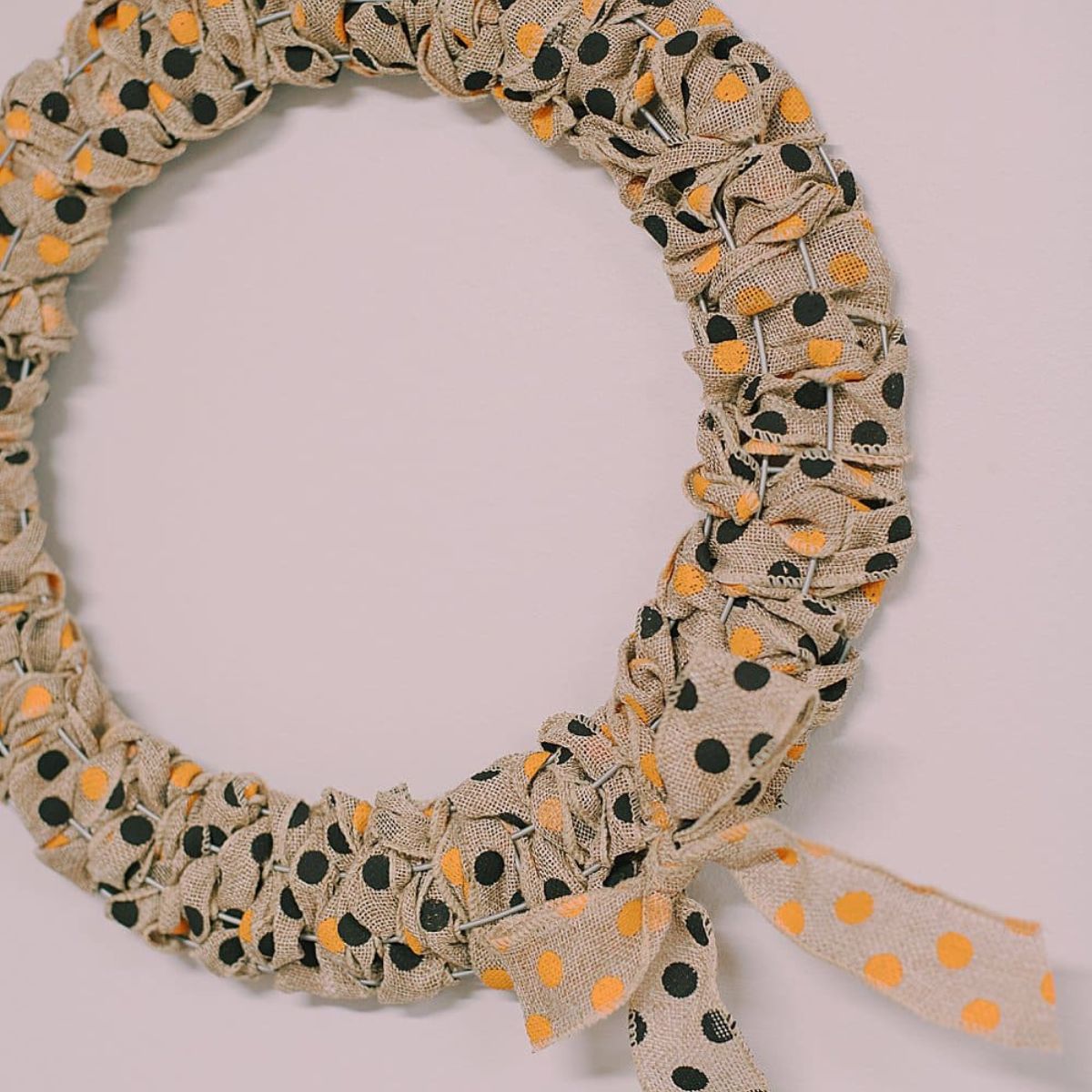 A Halloween wreath made with burlap ribbon with black and orange polka dots on it.